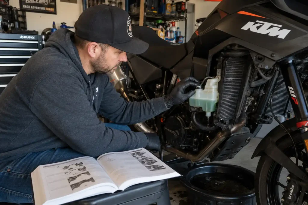 Is Motorcycle Coolant the Same as Car Coolant? 3 Rider performing motorcycle coolant maintenance with service manual open nearby